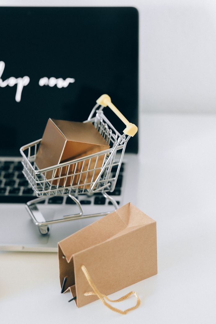 about-us-01 A miniature shopping cart with a parcel on a laptop symbolizes online shopping and e-commerce.
